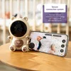 A baby monitor camera and a smartphone displaying a baby sleeping are on a wooden table. Produktbild-Vorschau