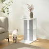 A white side table with gray felt accents is placed next to a sofa, with a cat walking in front of it. A vase with dried flowers and a cup of coffee are on top of the table. Produktbild-Vorschau