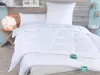 A neatly made bed with white bedding and pillows, a bedside table with a lamp, and a wooden headboard. Produktbild-Vorschau