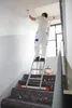 A painter is painting a wall on a ladder in a stairwell. Produktbild-Vorschau