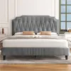 A gray upholstered bed frame with a tufted headboard is shown in a bedroom setting. Produktbild-Vorschau