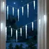 Icicle-shaped string lights are hung across a window at night, with trees visible outside. Náhled obrázku produktu