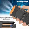 A hand holding a solar power bank with light beams emanating from it, suggesting it's a flashlight. Another view shows the device in a leather case. Produktbild-Vorschau