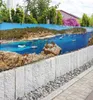 A scenic beach and harbor view printed on a fence banner, with a stone wall in the foreground. Produktbild-Vorschau