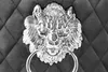 Close-up of a silver lion's head knocker with a ring, mounted on a dark, diamond-tufted fabric surface. Produktbild-Vorschau
