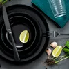 A table setting with black plates, cutlery, lime, and garlic. Náhled obrázku produktu
