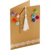 A close-up shot of a brown kraft paper greeting card decorated with colorful pom-poms and a white tassel. Náhľad obrázku produktu