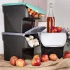 A still life arrangement of stacked storage containers for produce, with apples and a bottle of liquid in the foreground and background. Anteprima dell’immagine prodotto