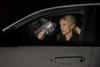A woman is in a car at night, holding a flashlight that is illuminating a broken car window. Produktbild-Vorschau