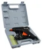 A black and orange hot glue gun is shown inside its gray plastic case, along with several glue sticks. Produktbild-Vorschau