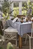 A table set for a meal outdoors, with a blue floral tablecloth, ceramic mugs, and a pitcher of water. Produktbild-Vorschau