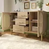 A light wood sideboard with cane detailing on the doors, displaying its drawers and shelving with decorative items. Podgląd zdjęcia produktu