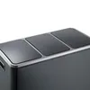A close-up view of the top of a dark gray multi-compartment trash can with a silver trim. Voir les images du produit