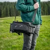 A person is carrying a black bicycle bag over their shoulder in a grassy field with trees in the background. Anteprima dell’immagine prodotto