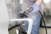 A person in blue jeans and a gray shirt, wearing blue gloves, is using a steam cleaner to clean a white chair. Steam is visibly coming from the steam cleaner. Voir les images du produit