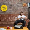 A man sits on a leather couch and uses his phone, with decorative items on the brick wall behind him. Produktbild-Vorschau