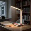 A desk lamp with a wireless charging pad is shown on a wooden desk next to an open book and a phone. Produktbild-Vorschau