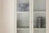 A close-up view of a beige vitrine with fluted glass doors, showcasing two shelves with decorative items. Voir les images du produit