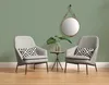 Two grey armchairs flank a small side table with a plant and a round mirror hanging on a green wall. Produktbild-Vorschau