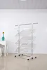 A white, multi-tiered drying rack with wheels is shown in a room with white tiled walls and floor. Produktbild-Vorschau