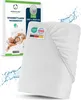 A white fitted sheet with elastic edges is shown diagonally, with a product box featuring a couple sleeping on a bed in the background. Water splashes are also depicted around the sheet. Náhled obrázku produktu
