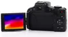The back view of a black Canon PowerShot digital camera with its LCD screen flipped out and displaying a colorful image. Produktbild-Vorschau