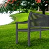 A park bench sits on a grassy lawn next to a body of water, with a tree and building in the background. Náhled obrázku produktu