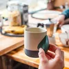 Keramiktasse "Climbing Mug Evo" von YY Vertical mit Klettergriff; auf einem Tisch mit weiteren Kletterutensilien. Podgląd zdjęcia produktu
