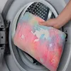 Mehrfarbige Decke mit Einhornmuster, die von einer Hand in eine Waschmaschine gelegt wird Produktbild-Vorschau