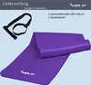 A purple yoga mat rolled up and unrolled, with a black strap, on a light gray background. Podgląd zdjęcia produktu