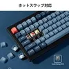 A close-up, angled view of a mechanical keyboard with some keys removed, showcasing the internal switches and keycaps. The keyboard is black with blue and gray keycaps, and a single red keycap is visible. Some loose keycaps are scattered around the keyboar Produktbild-Vorschau
