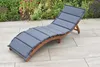 A wooden sun lounger with a gray cushion is placed on a paved patio next to a garden with plants. Náhled obrázku produktu