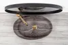 A top-down view of a marble sink with a gold faucet and drain, placed on a wooden surface, with a round mirror above it. Produktbild-Vorschau