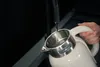 Water being poured into a white electric kettle with a stainless steel interior. Podgląd zdjęcia produktu