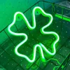 A green neon cloverleaf light is displayed inside a black wire basket. Produktbild-Vorschau