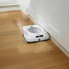 A white robotic vacuum cleaner is cleaning a wooden floor next to white cabinets. Anteprima dell’immagine prodotto