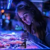 A young woman is looking into an aquarium, holding a device that appears to be a water filter or cleaning tool. Anteprima dell’immagine prodotto