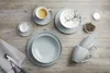 A collection of tableware, including cups, bowls, and plates, arranged on a wooden surface. Produktbild-Vorschau