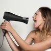 A woman is holding a black hairdryer to her mouth as if singing into it. Produktbild-Vorschau