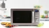 A Domo combi microwave oven is displayed on a countertop with a pie and a slice of cake in the foreground, and a blurred kitchen background. Náhled obrázku produktu