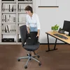 A woman is placing a black seat cushion on an office chair in an office setting. Produktbild-Vorschau