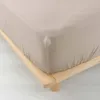 A close-up view of a beige fitted sheet on a wooden bed frame. Náhled obrázku produktu