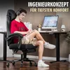 A young man is sitting in a gaming chair at a desk, wearing headphones and writing in a notebook. The desk has a computer monitor and other office supplies. The background is a modern office or home office setting. Produktbild-Vorschau
