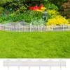 A white picket fence bordering a garden with green grass in the foreground and colorful flowers in the background. Náhľad obrázku produktu