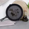A cast iron skillet with oil in it, next to a bottle of olive oil and a wooden slice. Produktbild-Vorschau