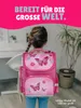 A young girl wearing a pink backpack with butterfly motifs stands in a room, facing away from the camera. Produktbild-Vorschau