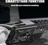 A black phone case with a ring holder is shown in a close-up shot, with a blurred background of a laptop and headphones. Produktbild-Vorschau