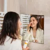 A woman in a bathrobe applies cream to her nose in front of a bathroom mirror. Anteprima dell’immagine prodotto