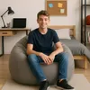 A young boy sits on a dark gray beanbag chair in a bedroom setting. Voir les images du produit