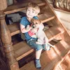 A young boy sits on wooden stairs holding a puppy. Produktbild-Vorschau